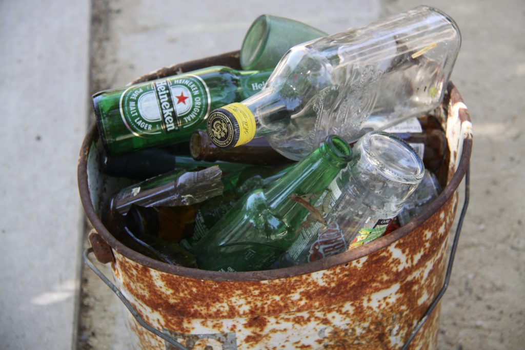 Seau rouillé collecté lors du ramassage des déchets, rempli de bouteilles de verre également collectées